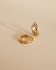 Gold hoop earrings with embedded stones on a beige background