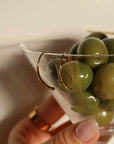Hand holding a martini glass filled with green olives against a neutral background