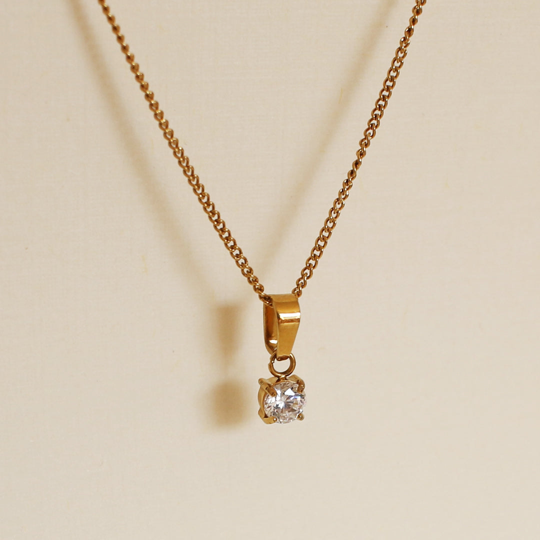 Gold necklace with a diamond pendant on a beige background