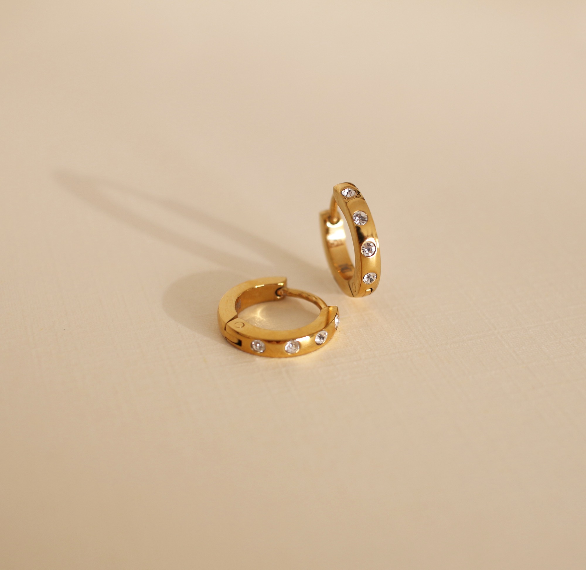 Gold hoop earrings with embedded stones on a beige background