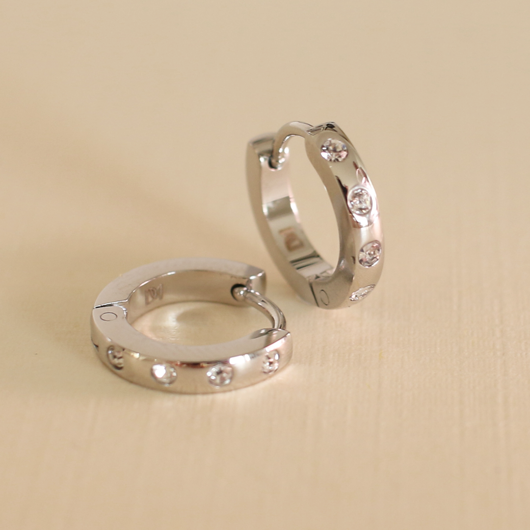 Pair of silver hoop earrings with embedded stones on a beige background