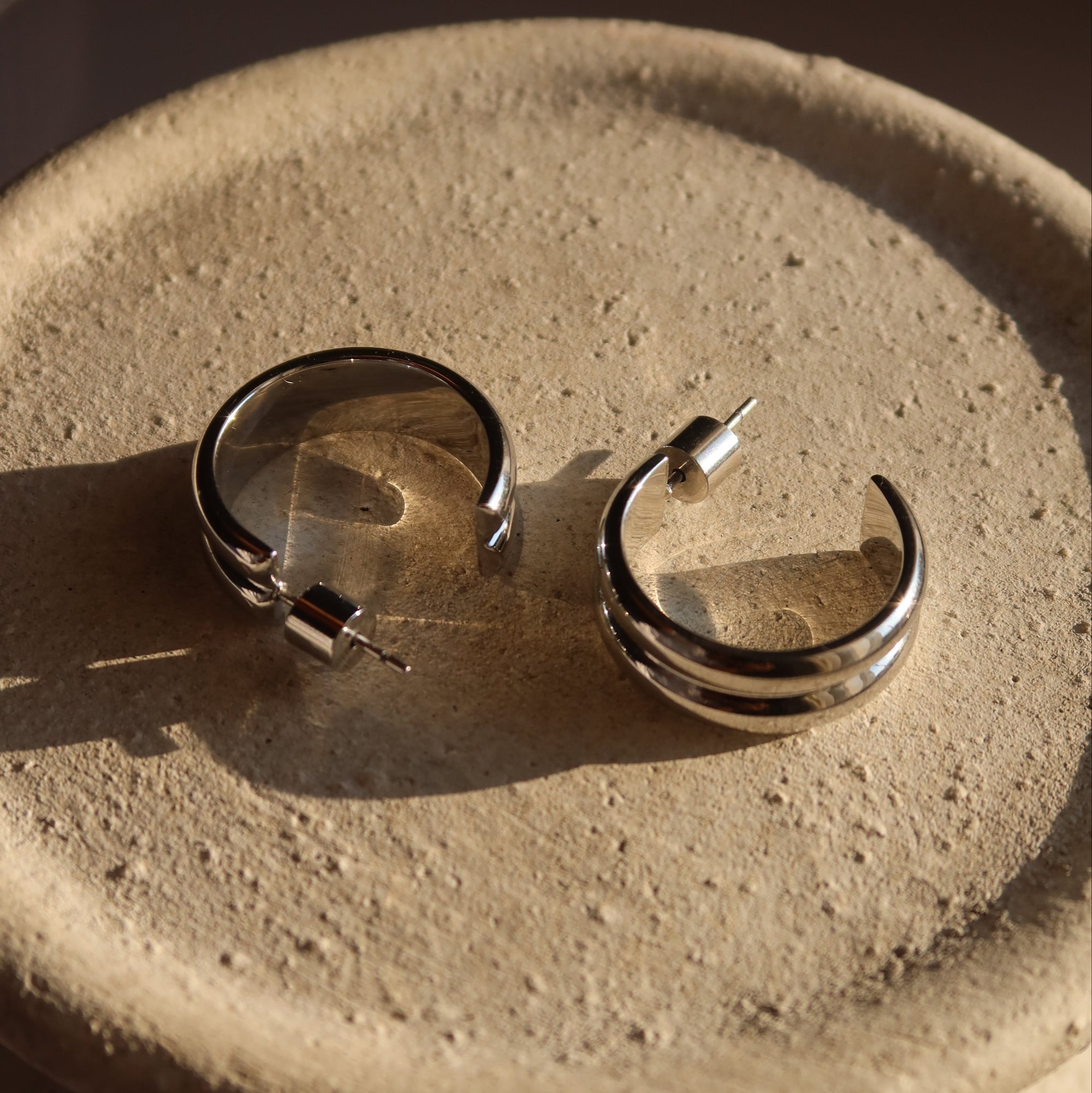 Pair of silver hoop earrings on a textured beige surface