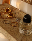 Gold earrings and rings on a marble surface with a Byredo perfume bottle.