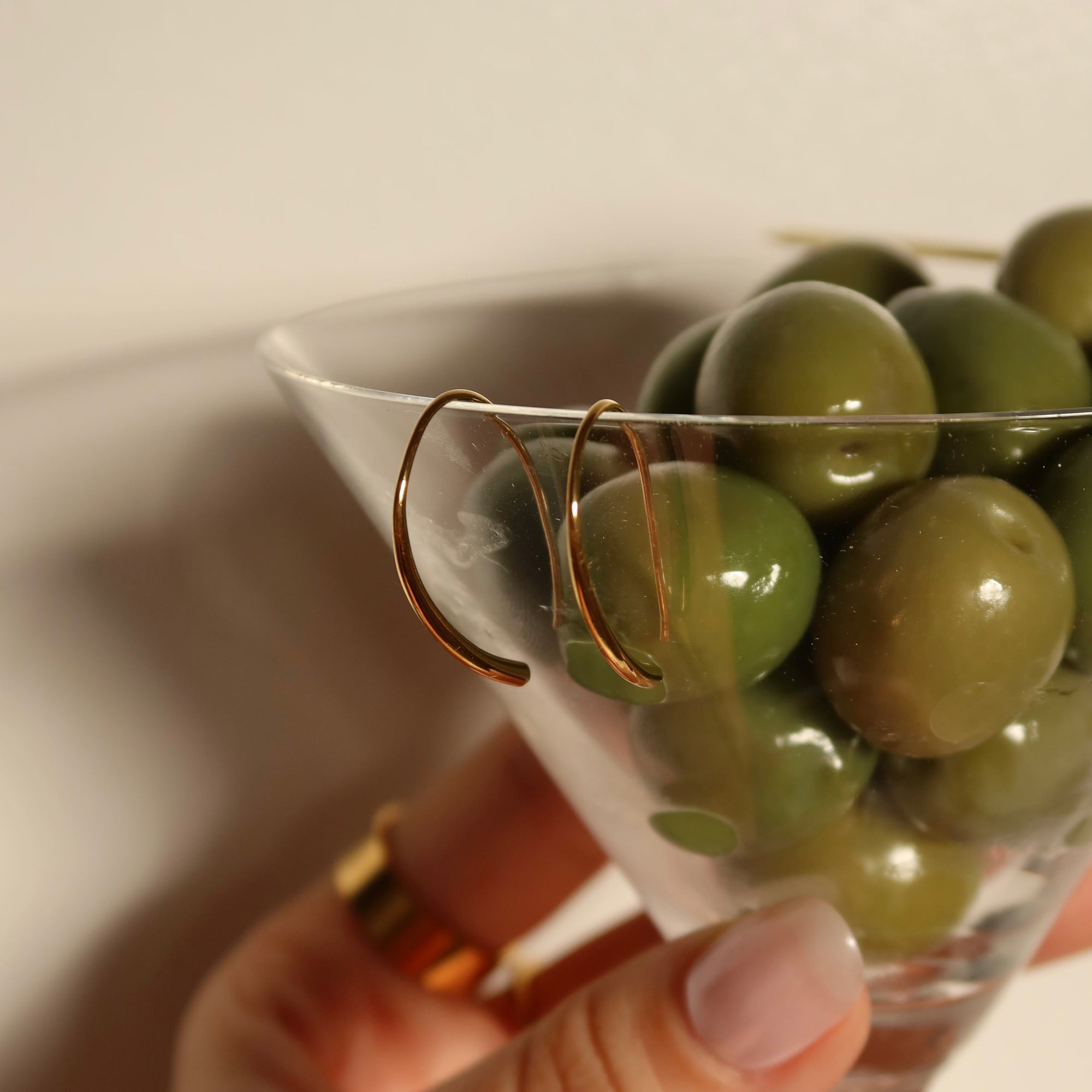 Hand holding a martini glass filled with green olives against a neutral background