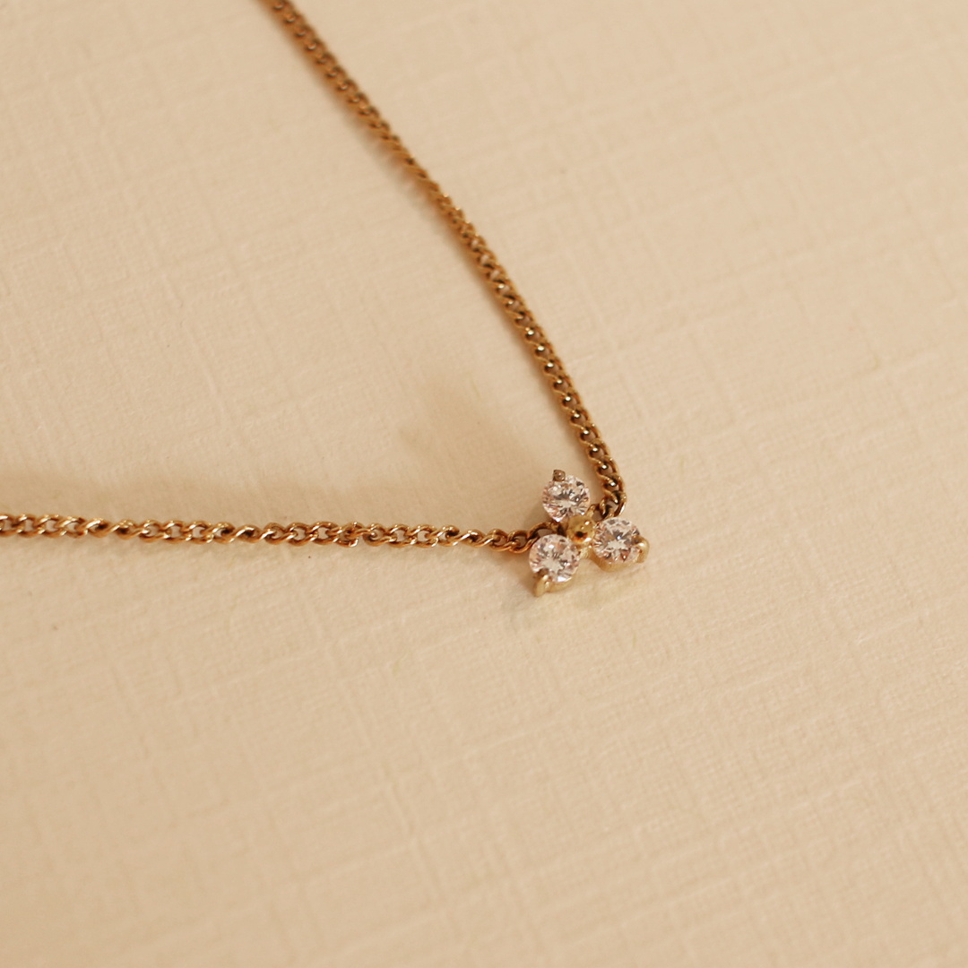 Gold necklace with a small three stone pendant on a beige background