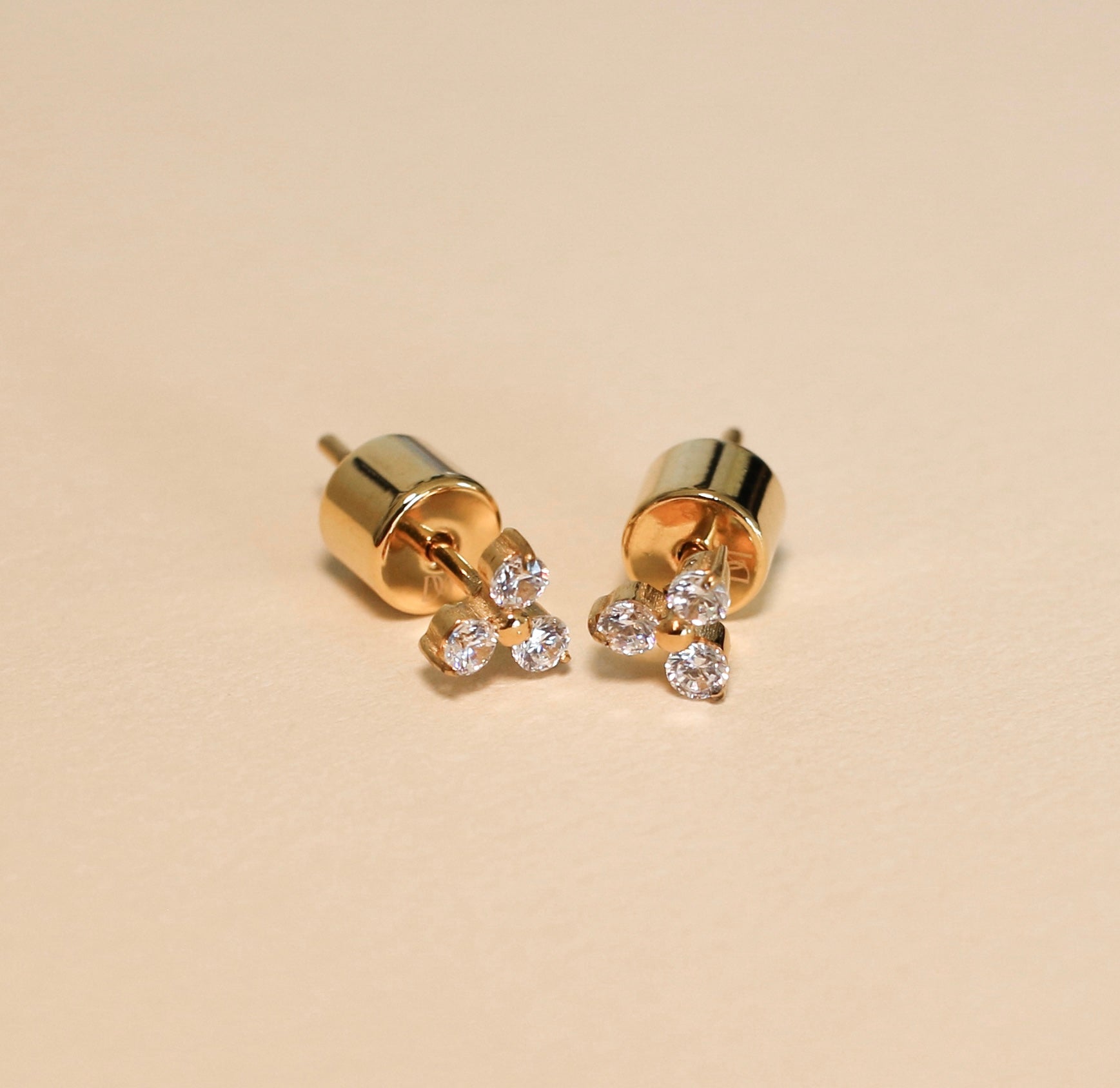 Gold earrings with small diamonds on a beige background