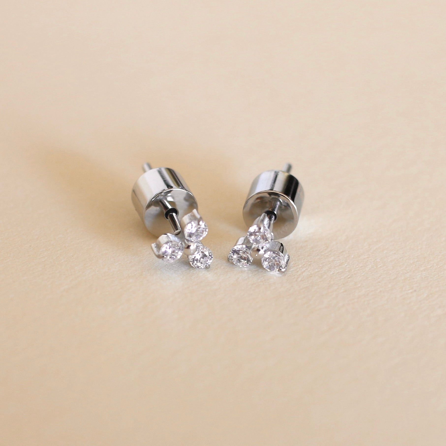 Silver earrings with small diamonds on a beige background